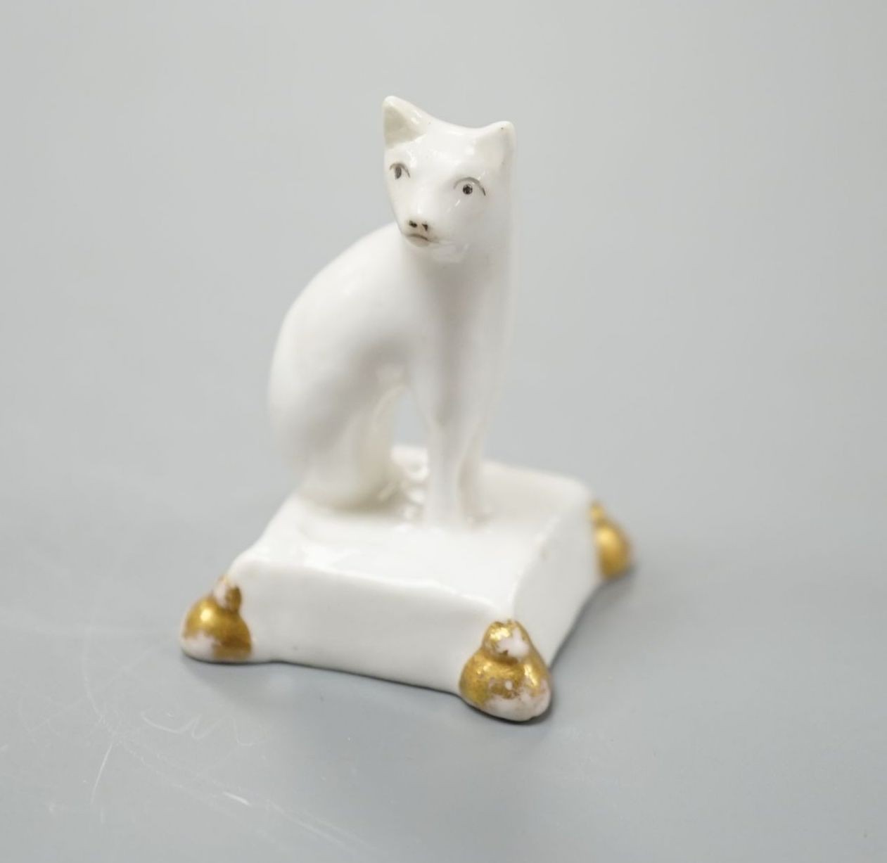 A rare English porcelain model of a cat seated on a cushion base, possibly Derby, c.1820-30, 4cm high, Provenance: Dennis G.Rice collection